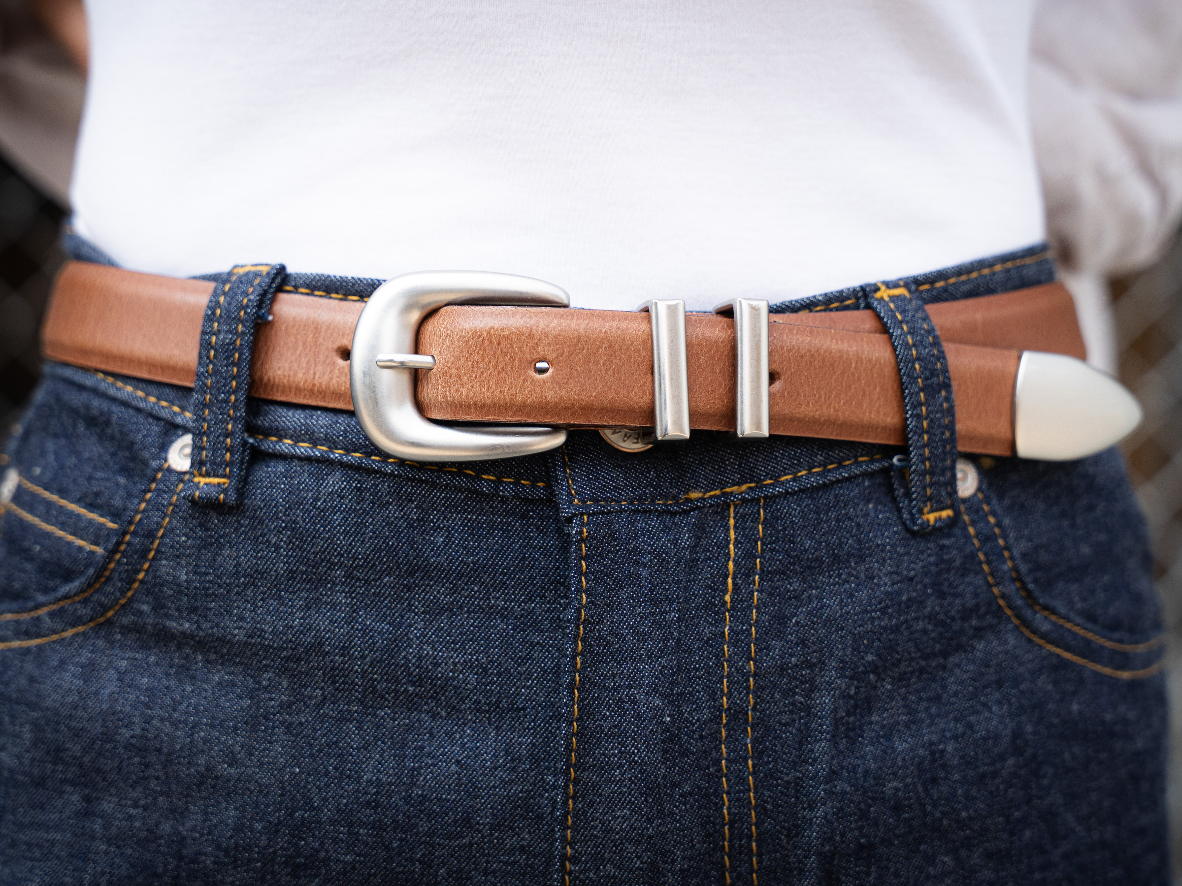 Close-up of a brown belt with a silver buckle on blue jeans.