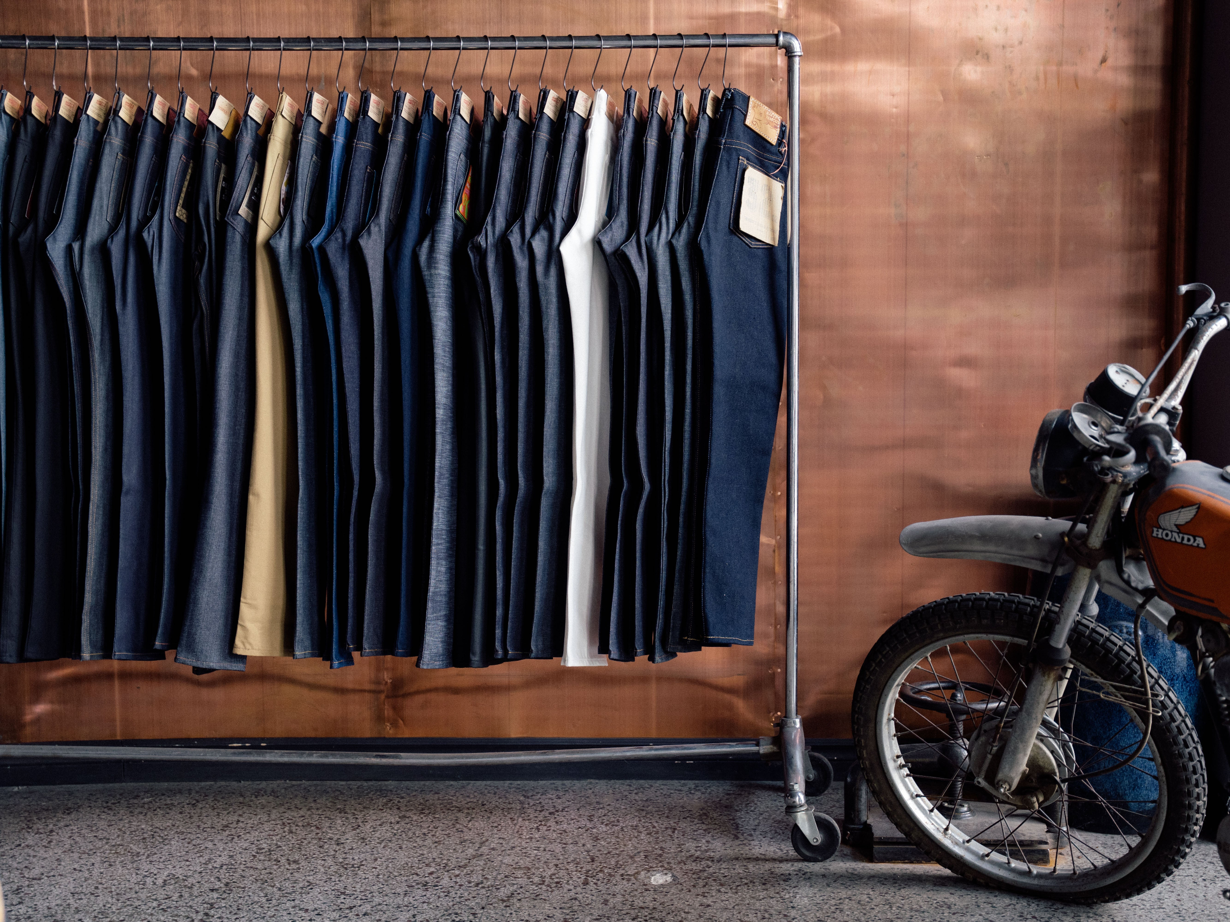 Row of pants on a rack with a motorcycle in the background. Inviting user to see fit guide.